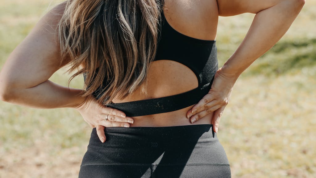 Close-up of a woman holding her back, suggesting back pain outdoors.